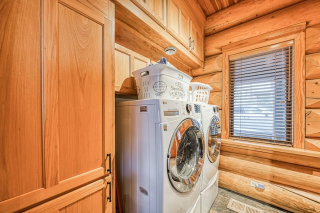 laundry area with log walls, washer and clothes dryer, cabinets, and wood walls