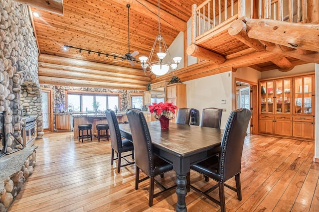 dining room featuring high vaulted ceiling, a fireplace, rustic walls, beam ceiling, and a chandelier