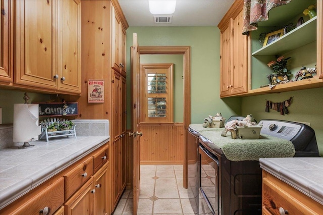 washroom featuring washer and clothes dryer, wood walls, cabinets, and light tile patterned floors