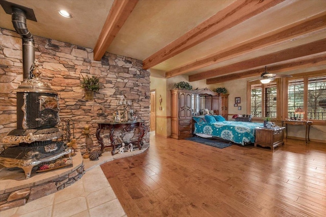 bedroom featuring beamed ceiling, light hardwood / wood-style flooring, and a wood stove