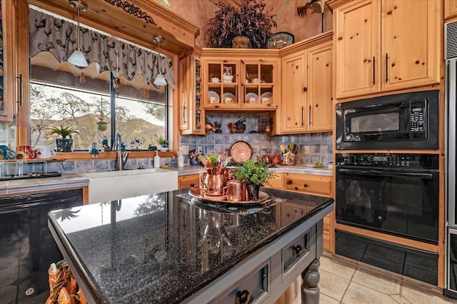 kitchen featuring dark stone counters, sink, black appliances, light tile patterned floors, and a center island