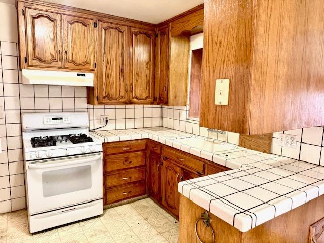 kitchen with kitchen peninsula, decorative backsplash, tile counters, and white gas range