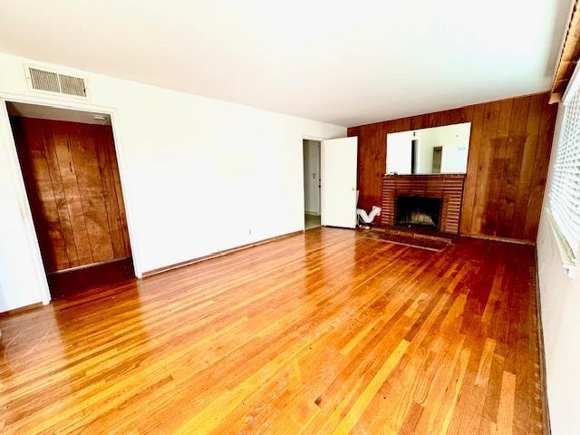 unfurnished living room with wooden walls, wood-type flooring, and a brick fireplace