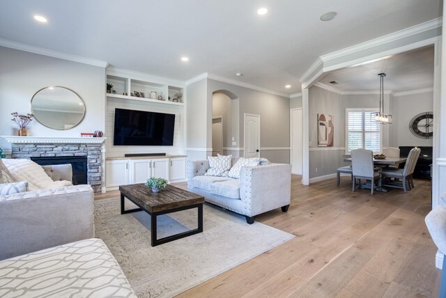 living room featuring a stone fireplace, built in shelves, light hardwood / wood-style floors, and ornamental molding