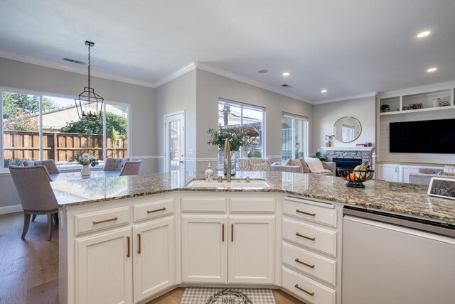 kitchen with plenty of natural light, white cabinets, a stone fireplace, sink, and a notable chandelier