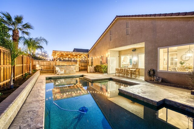 pool at dusk with a patio area, a bar, and an in ground hot tub