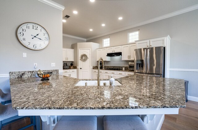 kitchen featuring a kitchen bar, stainless steel fridge, crown molding, sink, and white cabinets