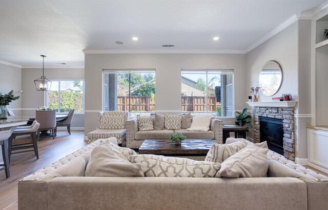 living room with a fireplace, ornamental molding, light wood-type flooring, and an inviting chandelier