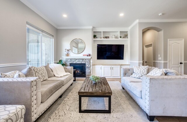 living room with crown molding, a fireplace, built in features, and light hardwood / wood-style flooring