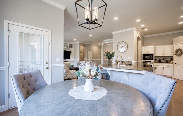 dining space featuring hardwood / wood-style flooring, an inviting chandelier, ornamental molding, and sink