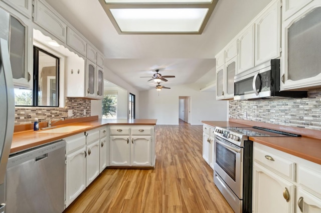 kitchen with ceiling fan, sink, stainless steel appliances, backsplash, and white cabinets