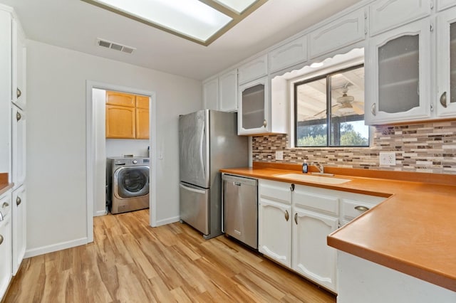 kitchen with stainless steel appliances, sink, light hardwood / wood-style flooring, washer / clothes dryer, and white cabinetry