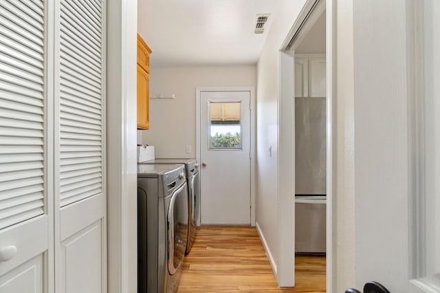 washroom featuring separate washer and dryer, light hardwood / wood-style flooring, and cabinets