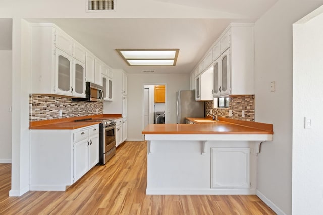 kitchen featuring white cabinets, sink, appliances with stainless steel finishes, tasteful backsplash, and kitchen peninsula