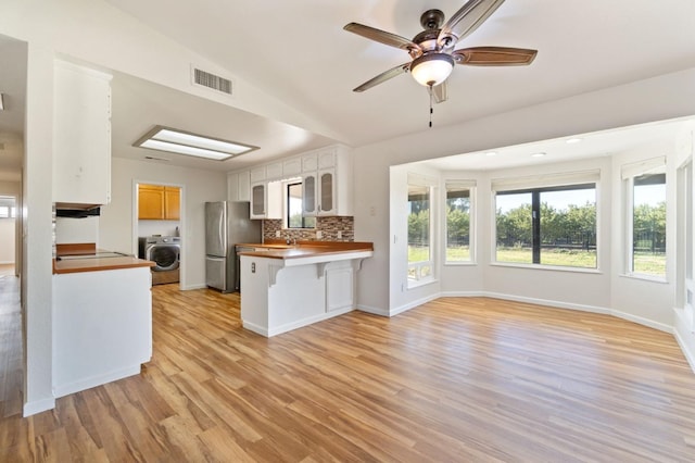 kitchen featuring kitchen peninsula, vaulted ceiling, washer / clothes dryer, white cabinetry, and stainless steel refrigerator