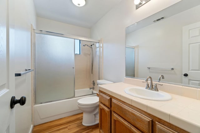 full bathroom featuring hardwood / wood-style flooring, vanity, toilet, and shower / bath combination with glass door