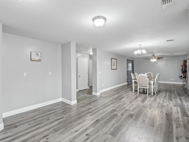 unfurnished dining area with hardwood / wood-style floors, ceiling fan with notable chandelier, and a textured ceiling