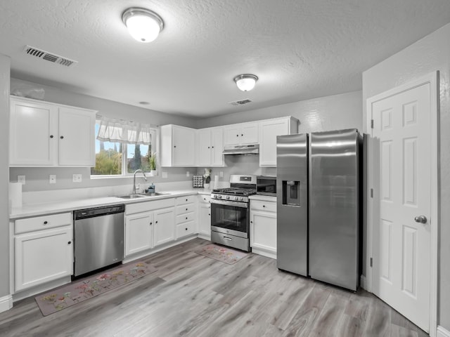 kitchen with appliances with stainless steel finishes, a textured ceiling, sink, white cabinets, and light hardwood / wood-style floors