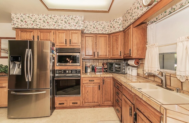 kitchen with built in microwave, sink, stainless steel refrigerator with ice dispenser, tile countertops, and black oven