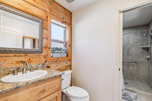 bathroom with a tile shower, wooden walls, vanity, and toilet