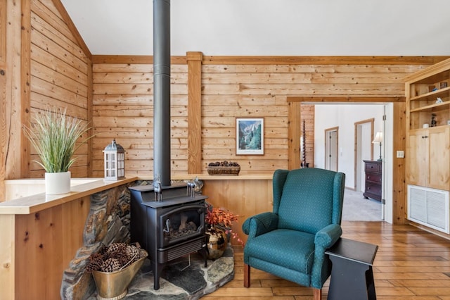 sitting room featuring a wood stove, wooden walls, wood-type flooring, and vaulted ceiling