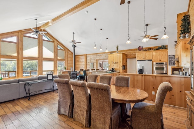 dining space featuring beam ceiling, light wood-type flooring, high vaulted ceiling, and wood walls