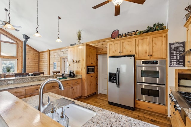 kitchen with stainless steel appliances, wooden walls, sink, decorative light fixtures, and lofted ceiling