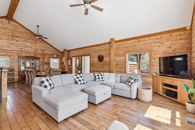 living room featuring beamed ceiling, light hardwood / wood-style flooring, ceiling fan, and wood walls