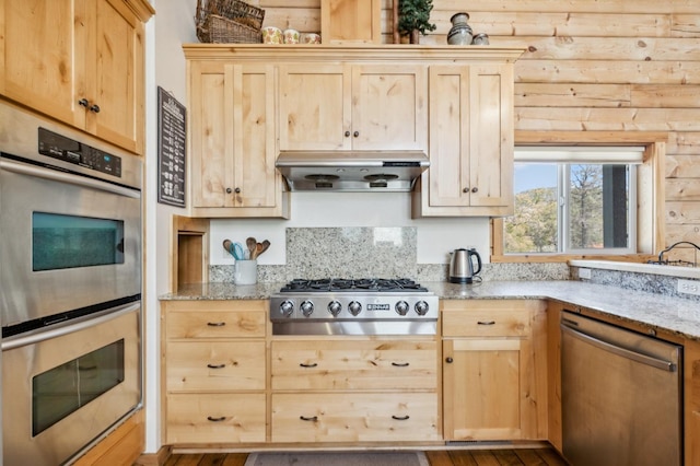 kitchen with light stone counters, light brown cabinetry, log walls, and appliances with stainless steel finishes