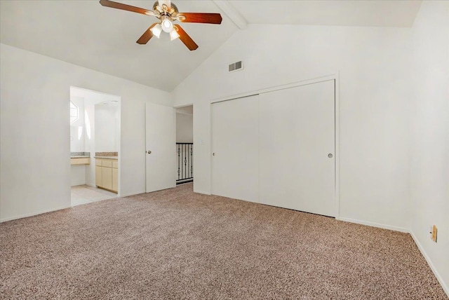 unfurnished bedroom with connected bathroom, ceiling fan, vaulted ceiling with beams, light carpet, and a closet