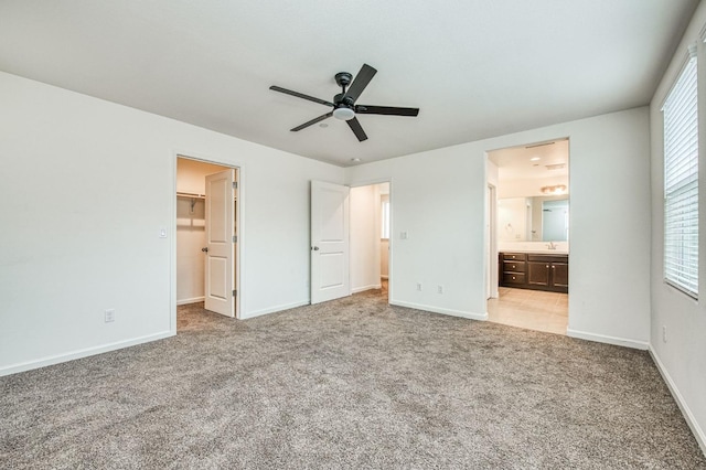 unfurnished bedroom featuring light carpet, a walk in closet, ensuite bathroom, ceiling fan, and sink