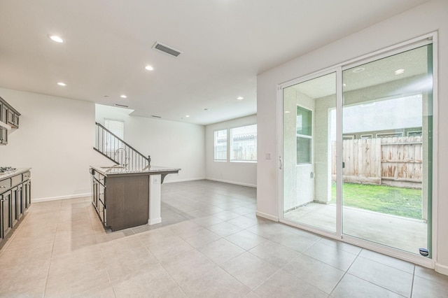 kitchen with sink, a kitchen breakfast bar, an island with sink, stainless steel gas stovetop, and light tile patterned flooring