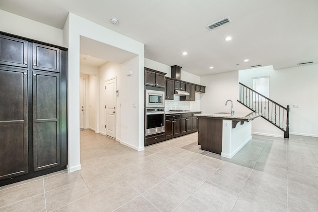 kitchen with stainless steel appliances, a kitchen breakfast bar, tasteful backsplash, a kitchen island with sink, and light tile patterned flooring