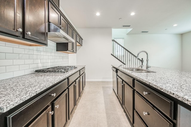 kitchen with light stone countertops, appliances with stainless steel finishes, dark brown cabinets, and sink