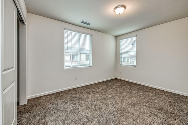 unfurnished bedroom with multiple windows, a closet, and dark colored carpet