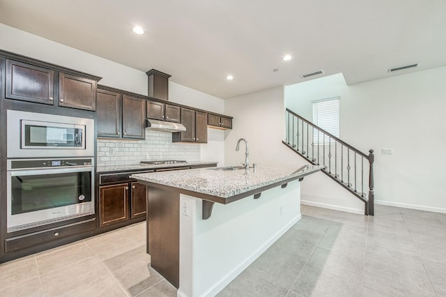 kitchen featuring dark brown cabinetry, stainless steel appliances, a kitchen island with sink, and sink