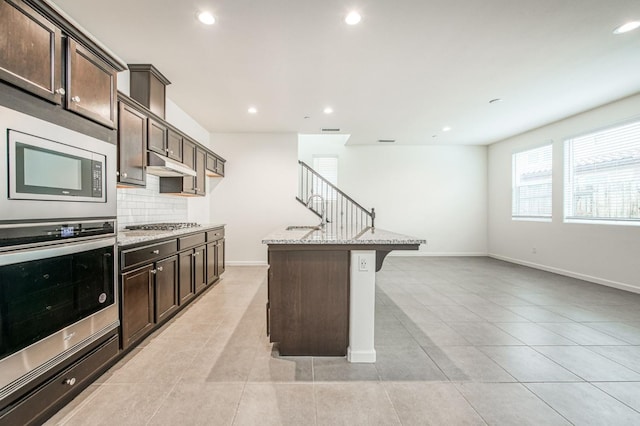 kitchen featuring a center island with sink, dark brown cabinetry, light stone countertops, and stainless steel appliances