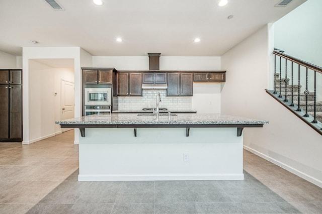 kitchen with a kitchen breakfast bar, dark brown cabinetry, stainless steel appliances, and an island with sink