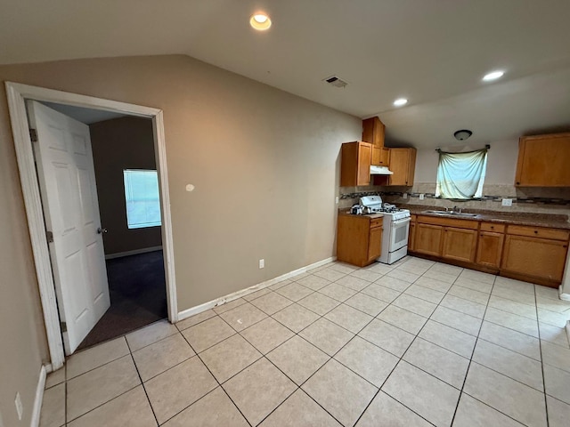 kitchen featuring sink, white gas stove, vaulted ceiling, light tile patterned floors, and backsplash