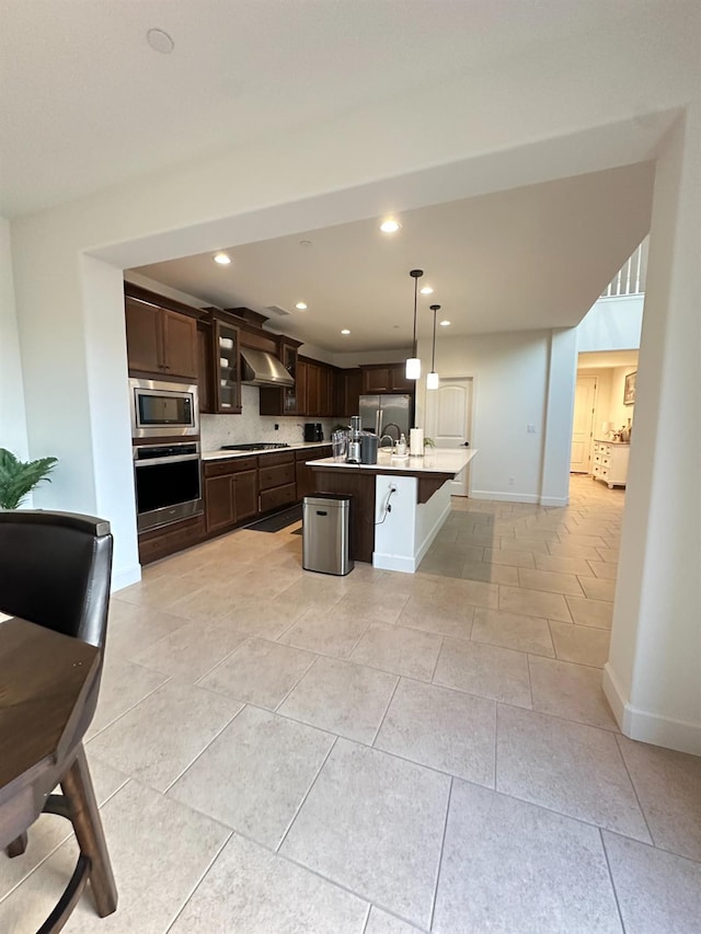 kitchen featuring wall chimney exhaust hood, dark brown cabinets, a kitchen island with sink, and appliances with stainless steel finishes