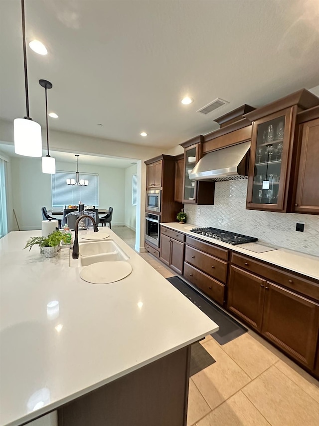 kitchen with a kitchen island with sink, extractor fan, hanging light fixtures, sink, and stainless steel gas cooktop