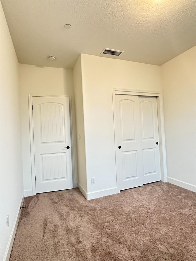 unfurnished bedroom featuring a textured ceiling, carpet floors, and a closet