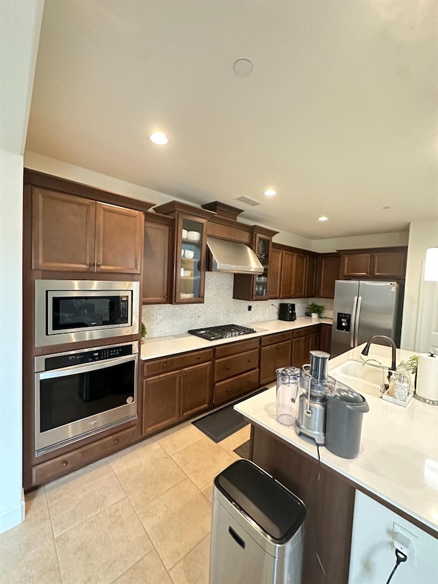 kitchen with exhaust hood, appliances with stainless steel finishes, tasteful backsplash, light tile patterned flooring, and dark brown cabinetry