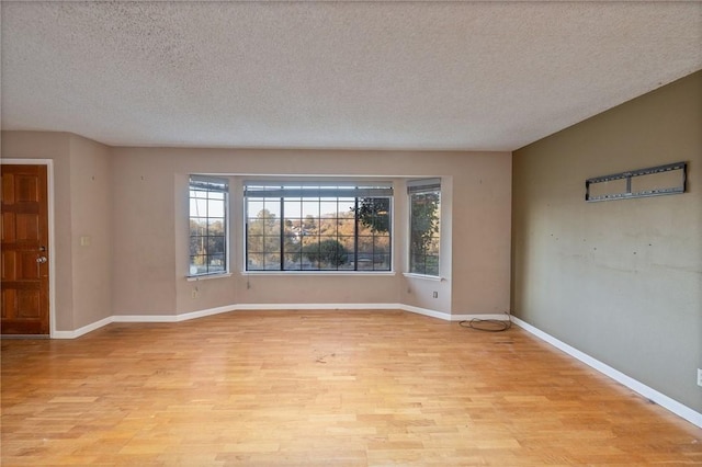 empty room featuring baseboards, light wood-style floors, a healthy amount of sunlight, and a textured ceiling