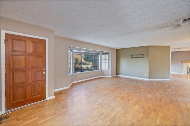 interior space featuring visible vents, baseboards, a textured ceiling, and light wood finished floors