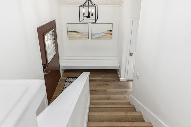 stairs with hardwood / wood-style flooring, crown molding, and a chandelier