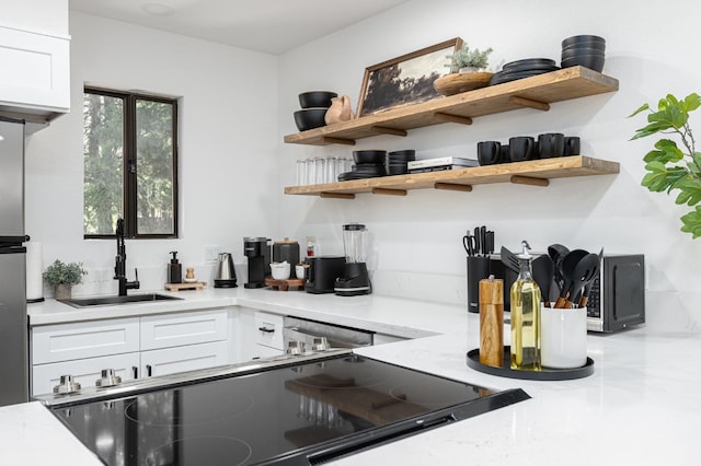 kitchen featuring white cabinets, light stone counters, stainless steel dishwasher, and sink