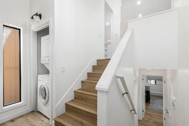 stairway with hardwood / wood-style floors, a baseboard radiator, and stacked washer and clothes dryer