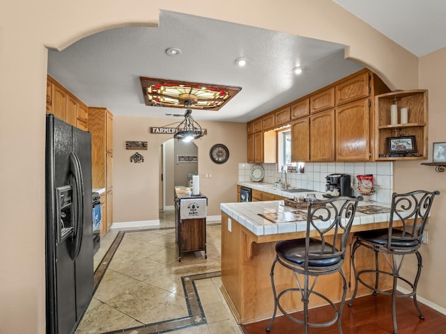 28899 Limestone Way, Coarsegold, CA 93614 - kitchen with black fridge with ice dispenser, a peninsula, arched walkways, tile countertops, and baseboards