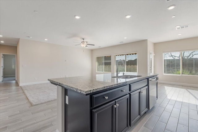 kitchen featuring light stone counters, ceiling fan, sink, dishwasher, and an island with sink